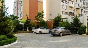 Ein Parkplatz mit zwei Autos, umgeben von Grünflächen und hohen Gebäuden.