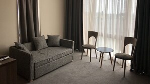 Una sala de estar moderna con un sofá gris, dos sillones, una mesita redonda y cortinas translúcidas.