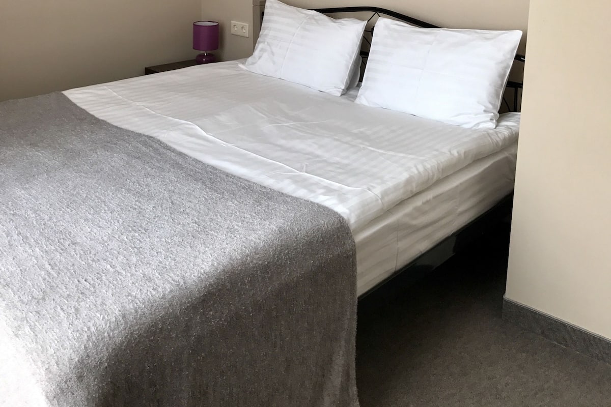 A neatly made bed with white linens, a gray throw blanket, and a colorful abstract painting on the wall.
