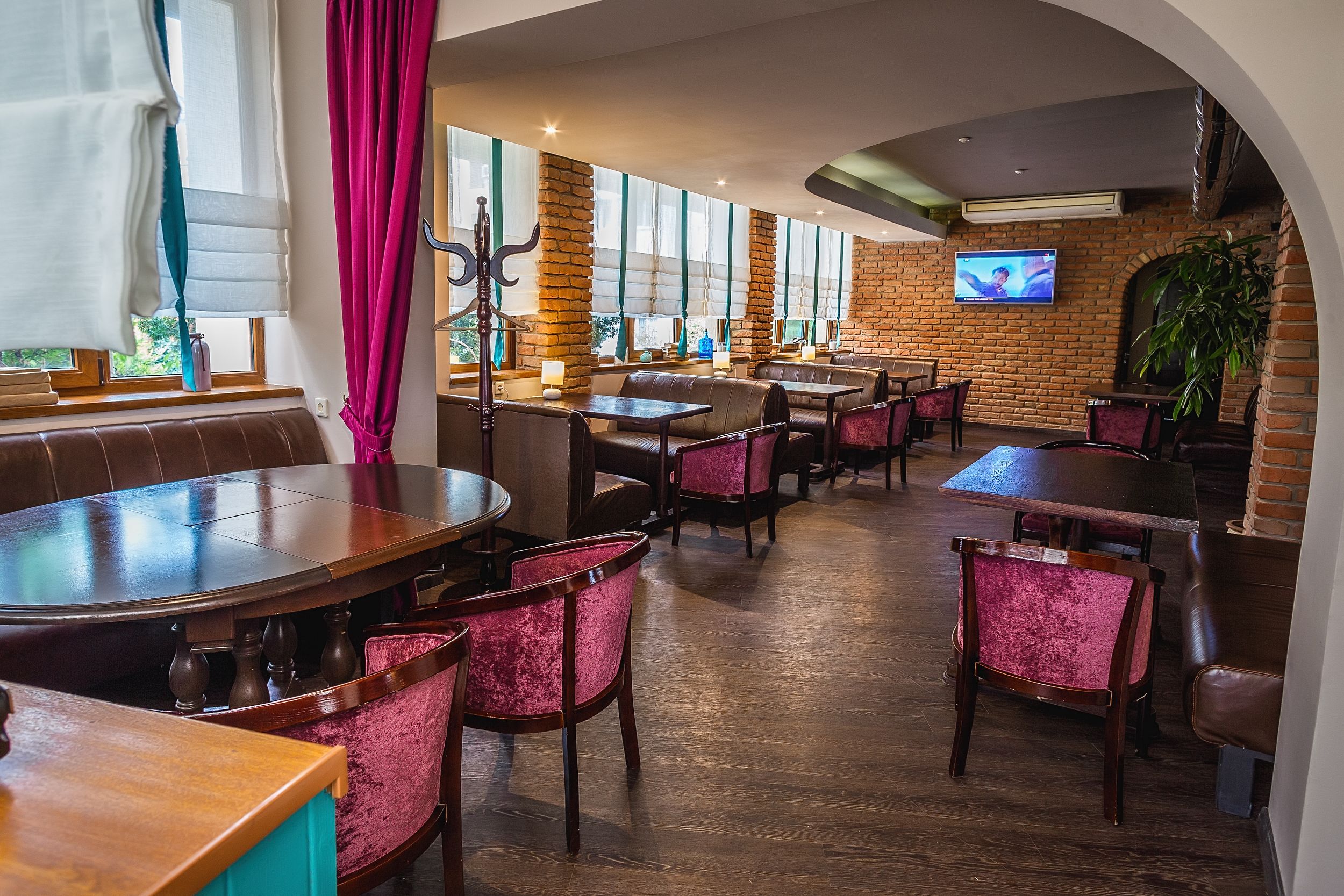 A restaurant with brick walls, large windows, and a TV screen.