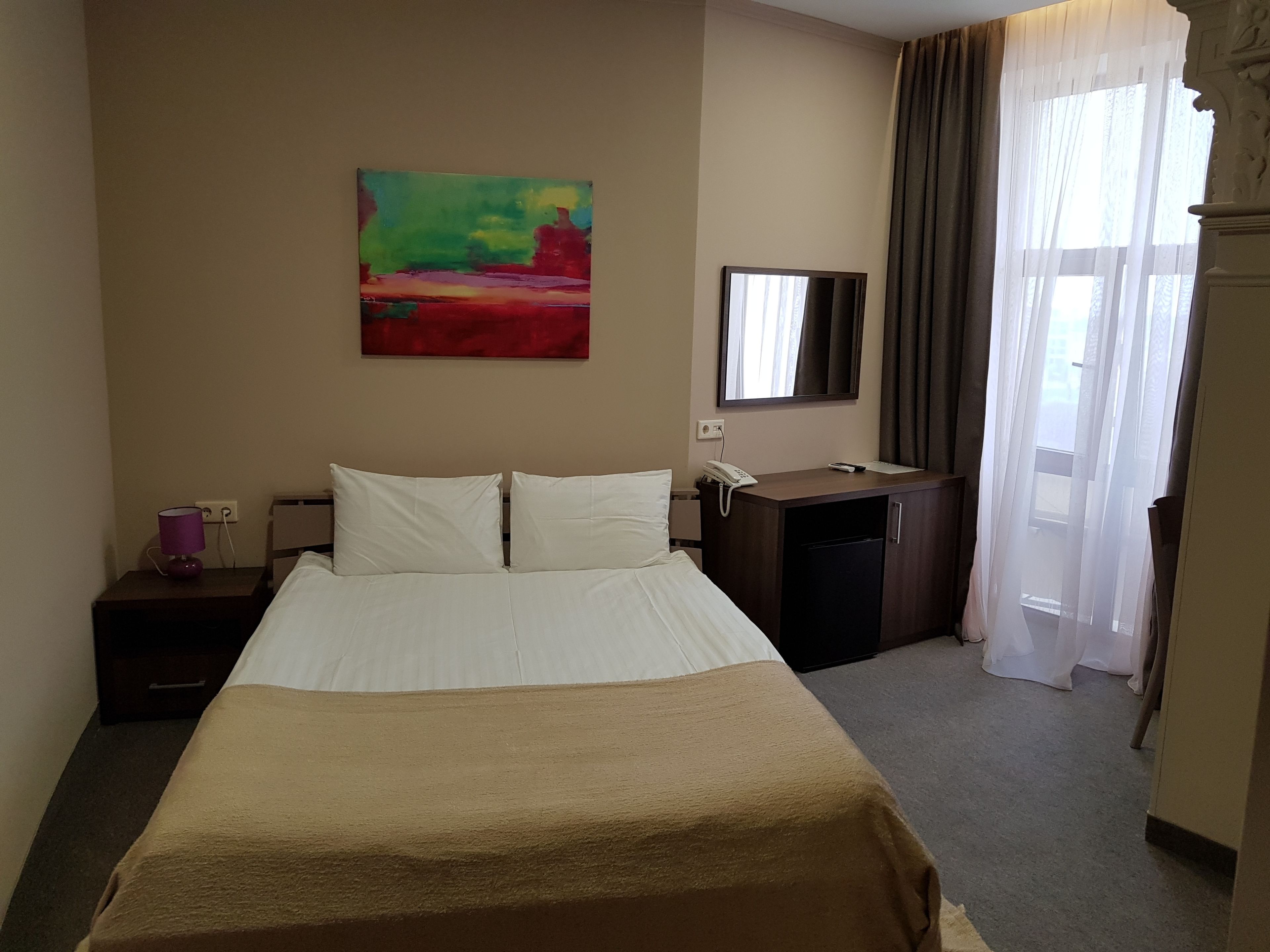 Una habitación de hotel con una cama, un escritorio, un teléfono y un cuadro en la pared.