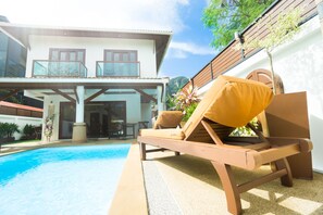 A modern house with a pool, a lounge chair, and a wooden deck.