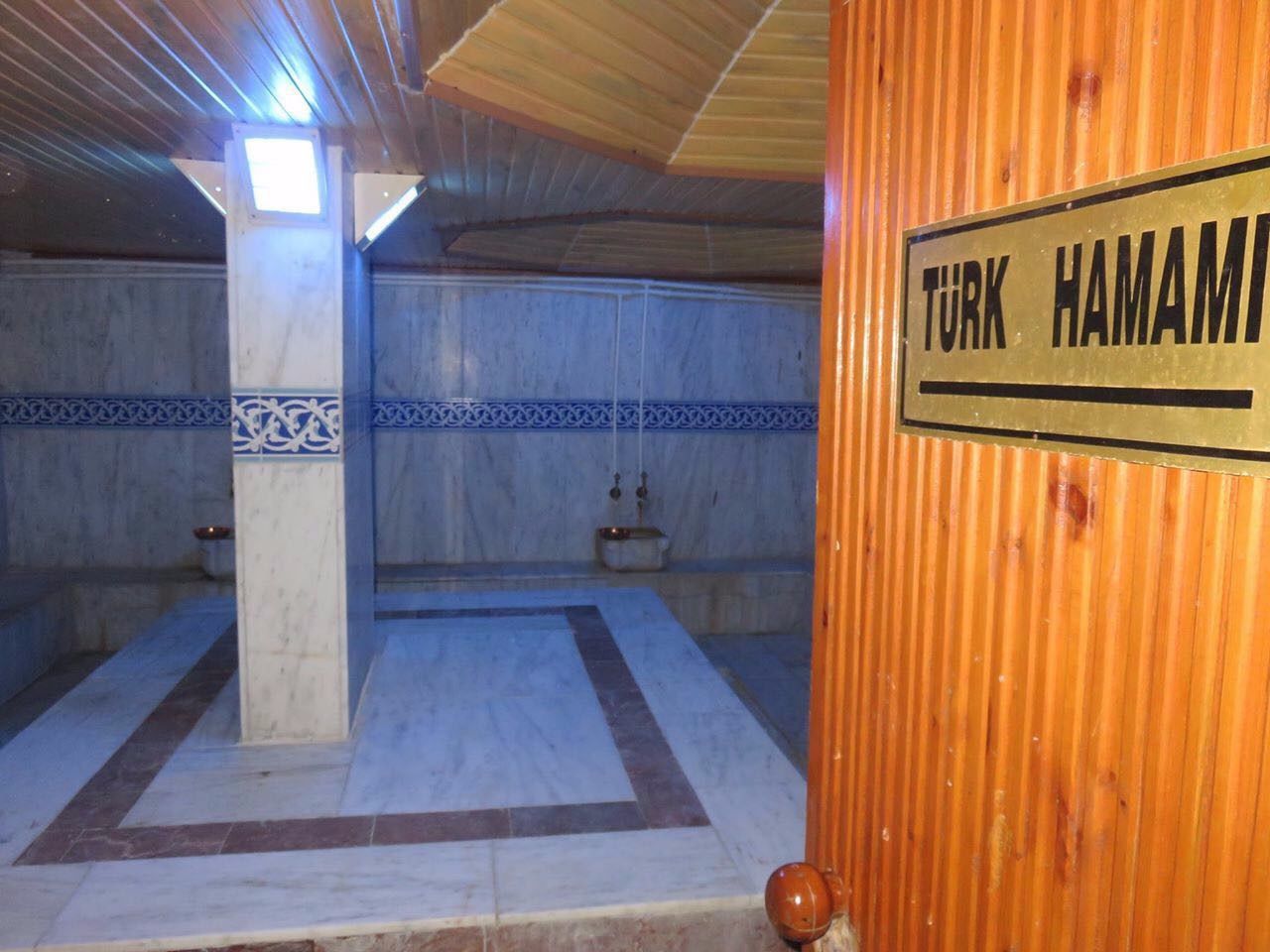 A room with a tiled floor, a wooden ceiling, and a sign reading "TURK HAMAMI".