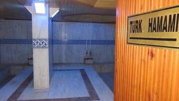 A room with a tiled floor, a wooden ceiling, and a sign reading "TURK HAMAMI".