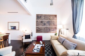 A modern living room with a high ceiling, a large wall-mounted map, a wooden coffee table, a sofa, and a dining area with a chair and table. - Rent In Rome - Flo's Apartment (Rome)