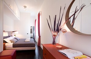 A modern hotel room with a bed, bedside table, lamp, and a decorative mirror. - Rent In Rome - Flo's Apartment (Rome)