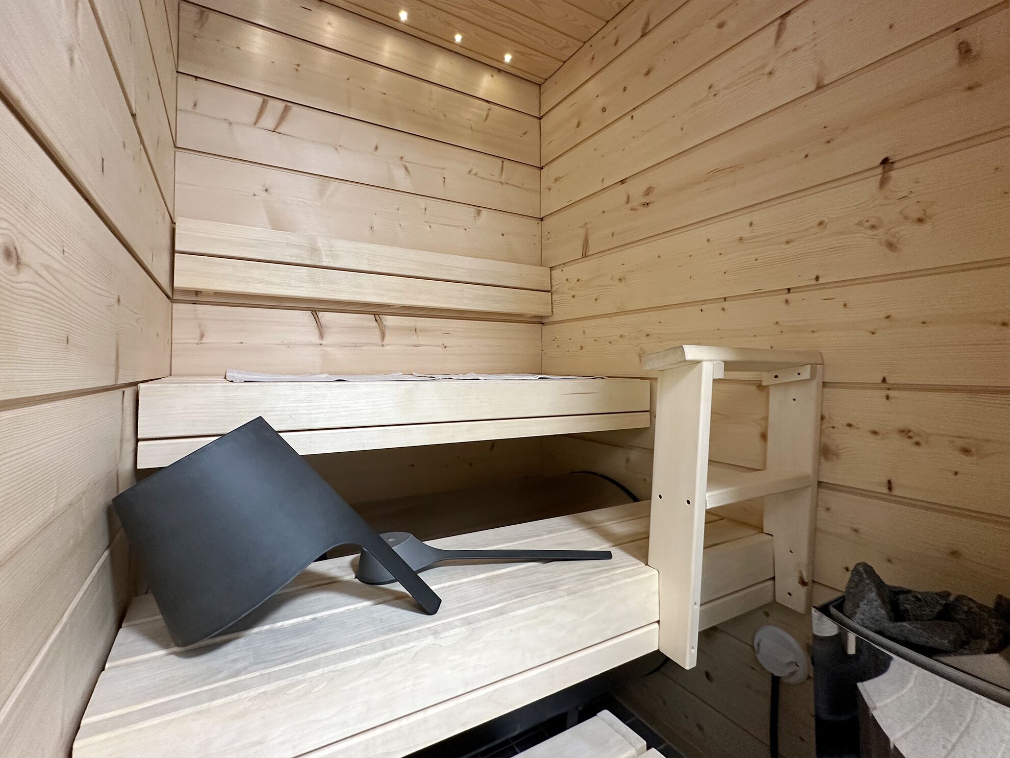 A wooden cabin interior with a bunk bed, a small table, and a trash bin.