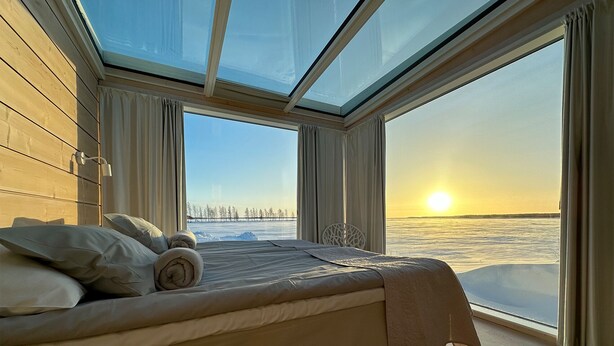 Camera da letto con un letto grande, un lucernario e vista su un paesaggio ghiacciato al tramonto.