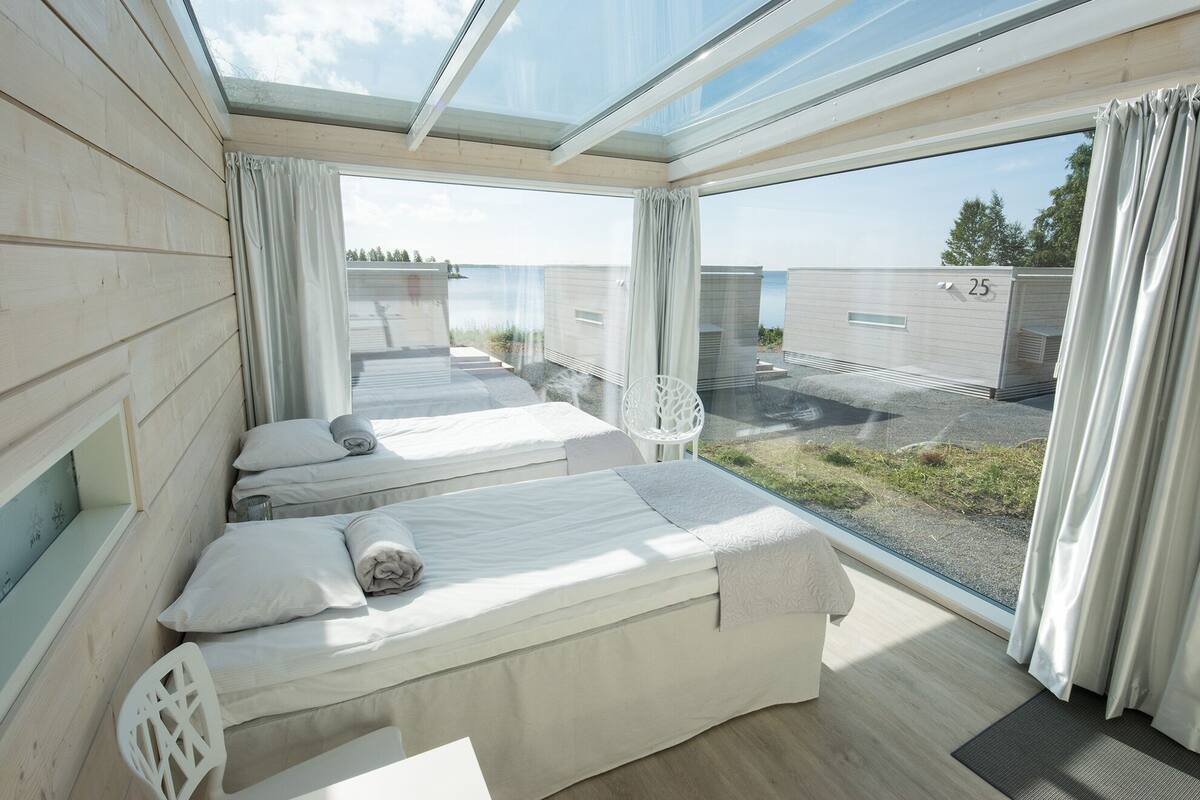 Un dormitorio moderno con un tragaluz grande, dos camas y vistas al área exterior.