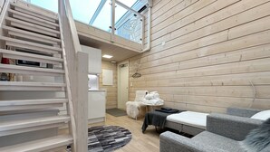 Un interno moderno con pavimento in legno, una scala, un divano, un tavolino e vista sul cielo tramite un lucernario.