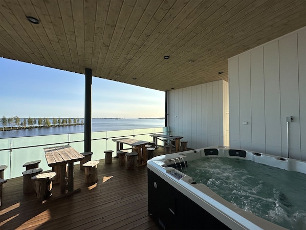 A wooden deck with a hot tub and tables overlooking a body of water.