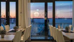 Un ristorante con vista sul tramonto su un corpo d'acqua, ampie vetrate e un design interno moderno.