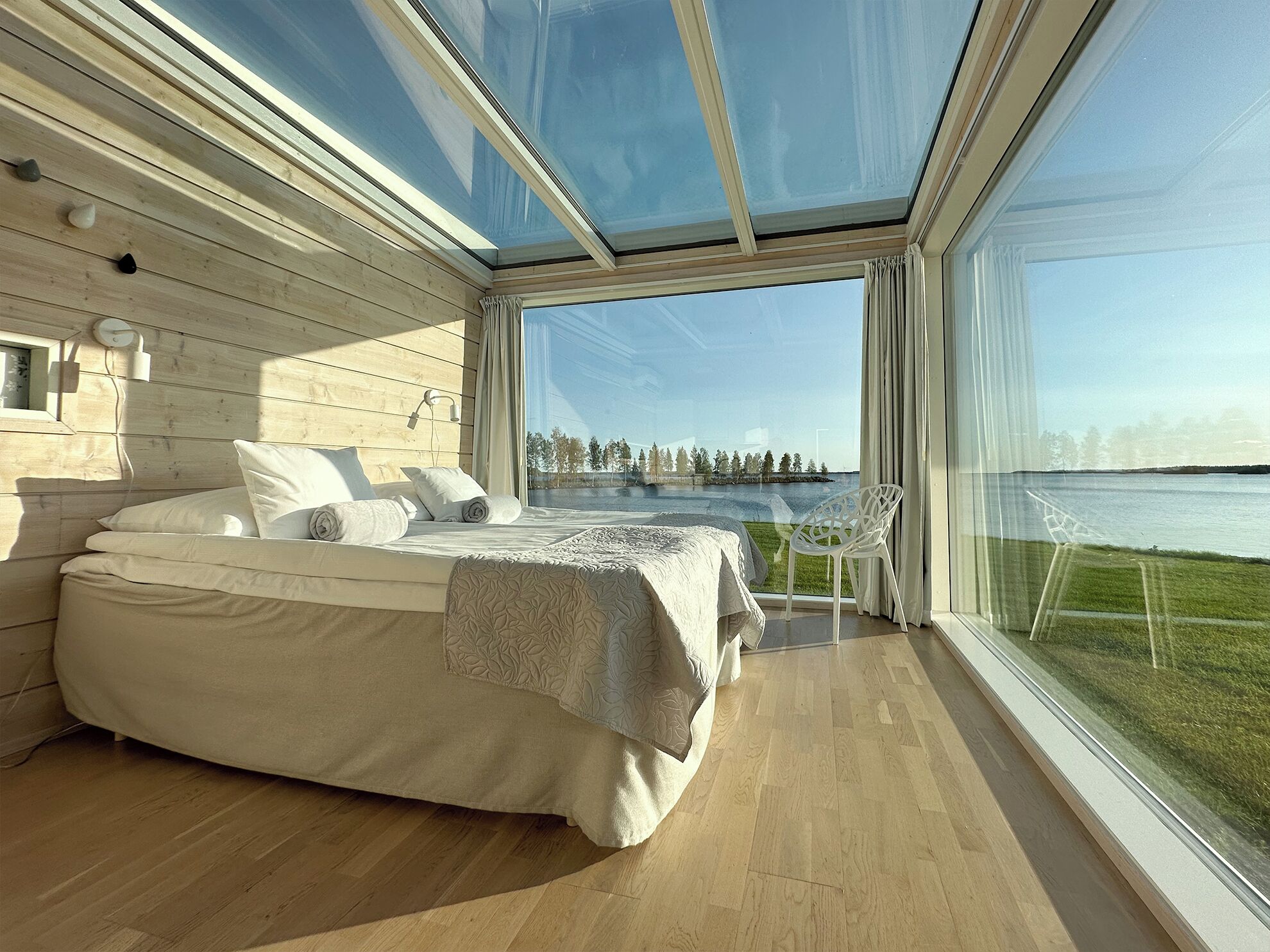 A modern bedroom with a large bed, a view of a lake, and a glass ceiling.