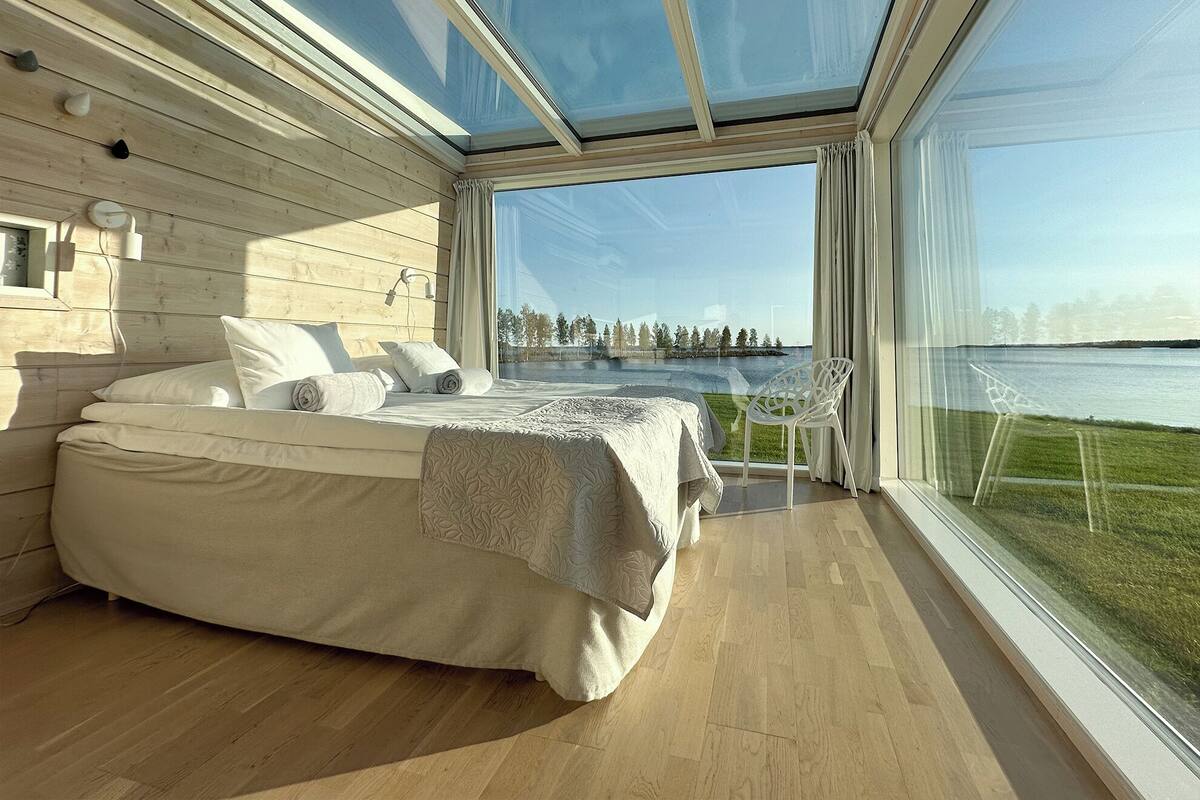 Un dormitorio moderno con una cama grande, vistas a un lago y techo de cristal.