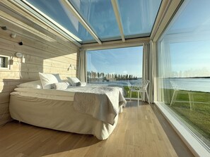 A modern bedroom with a large bed, a view of a lake, and a glass ceiling.