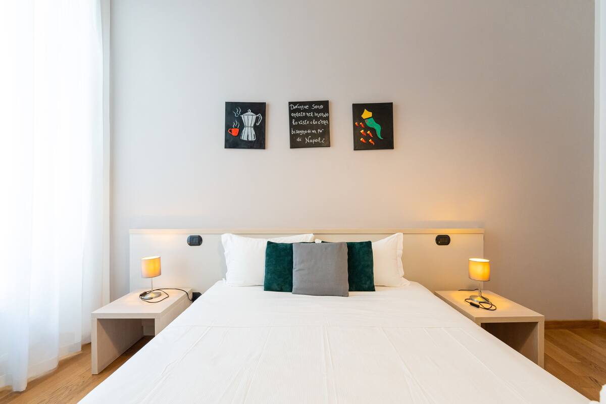 A neatly made bed with white bedding, two bedside tables with lamps, and three wall art pieces.