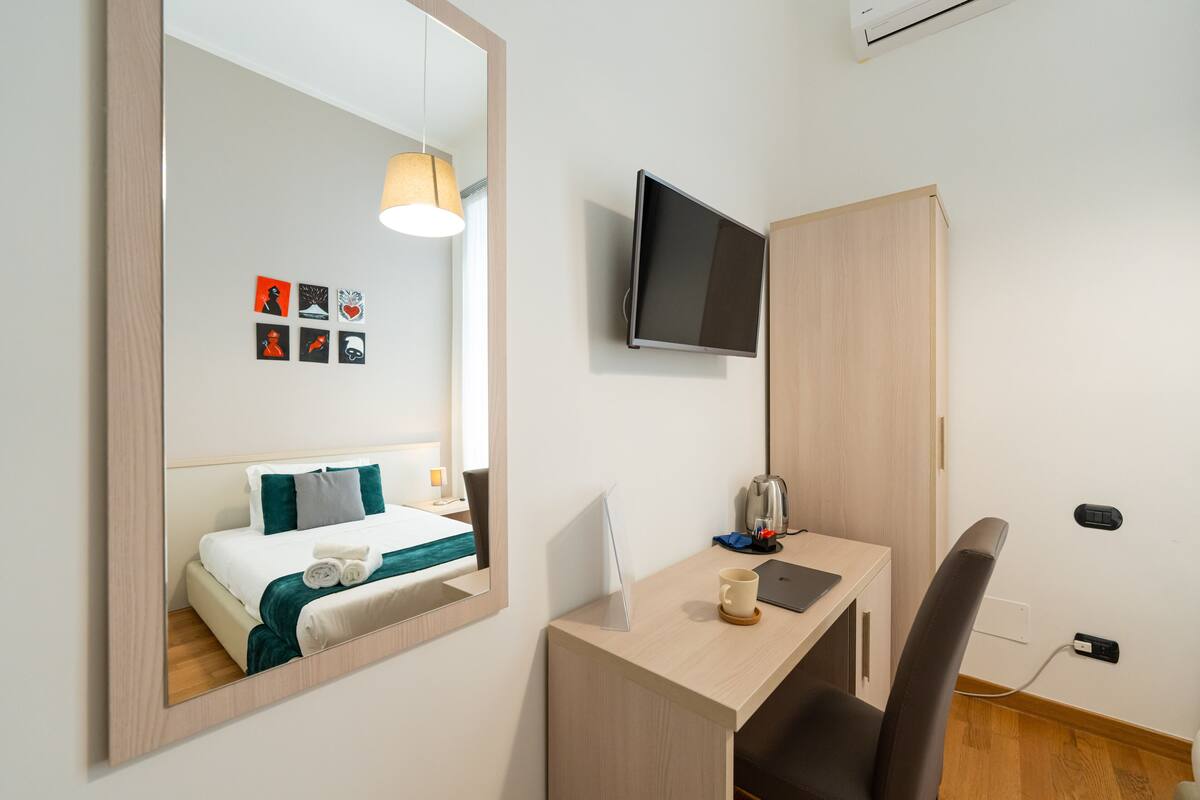 A hotel room with a bed, a desk, a chair, a TV, and a mirror.