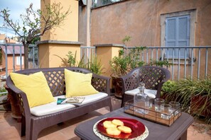 A patio with a wicker sofa and armchair, a tray with glasses and a plate of food, and a potted plant. - Rent In Rome - Vittoria Terrace (Rome)