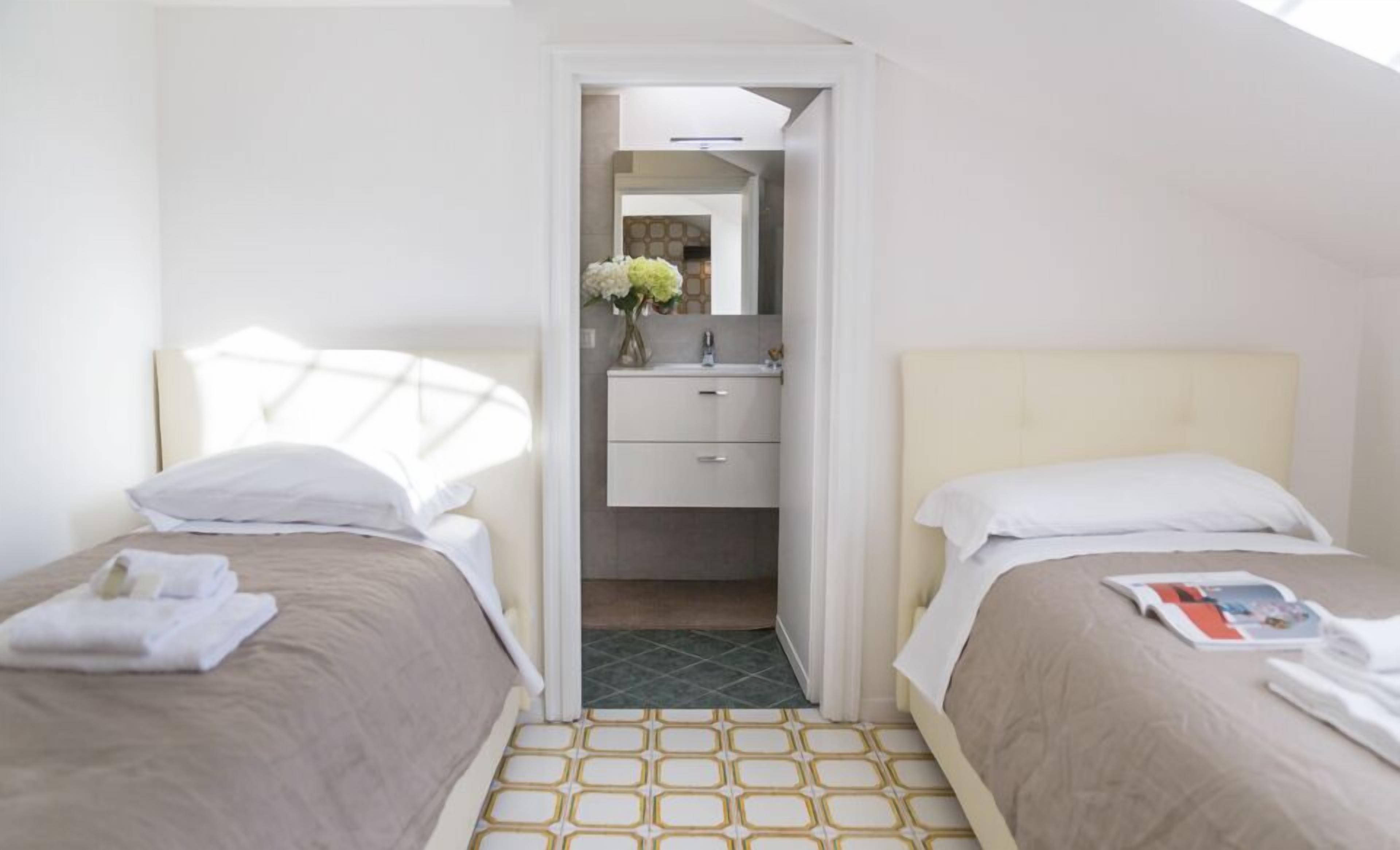 Habitación de hotel con dos camas, un baño pequeño y suelo de baldosas.