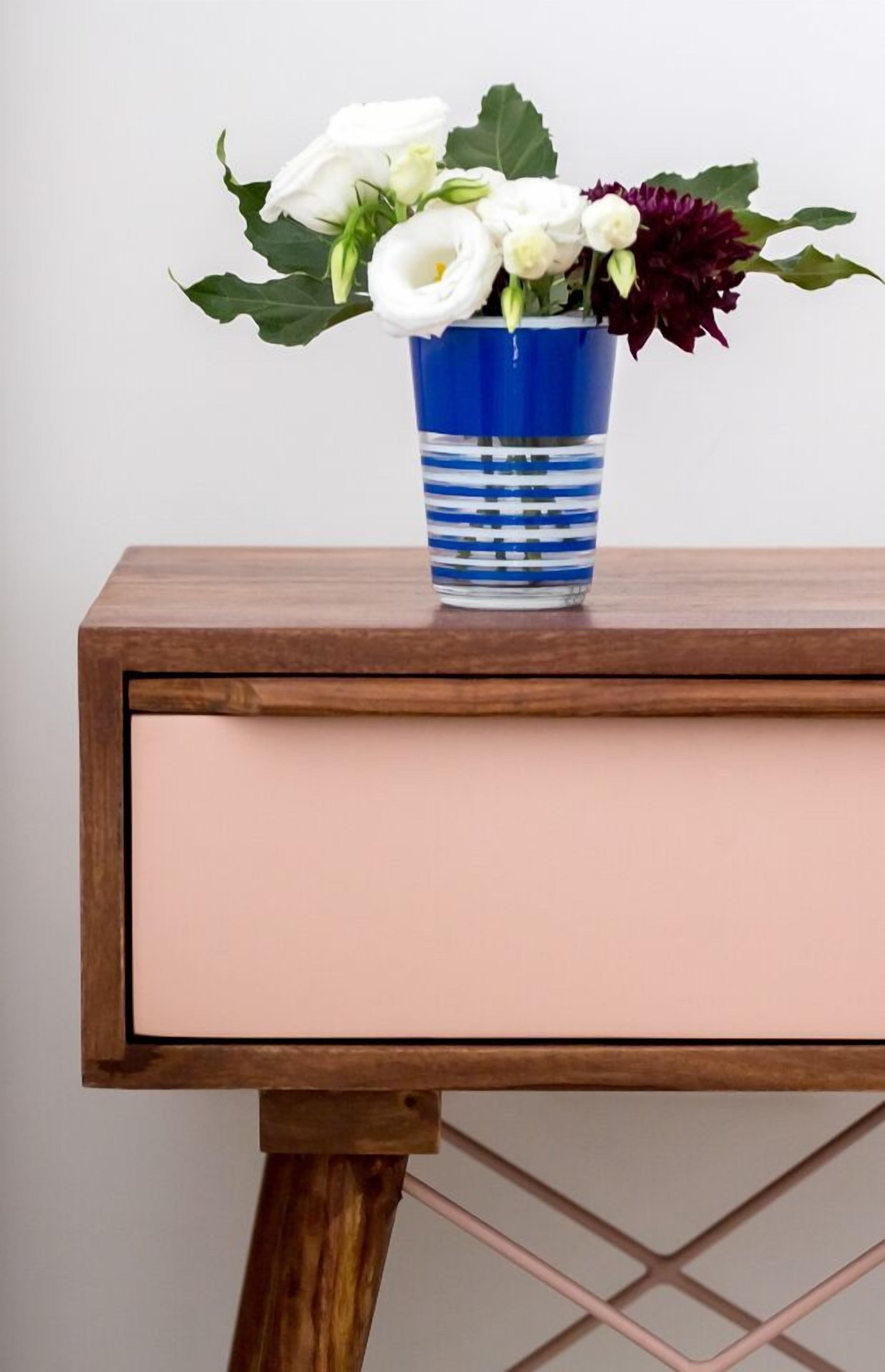 A wooden side table with a blue vase containing white and purple flowers.