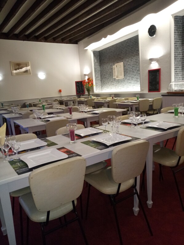 A dining area with tables set for meals, chairs, and a brick wall with a window. - Hôtel Moderne (Vichy)