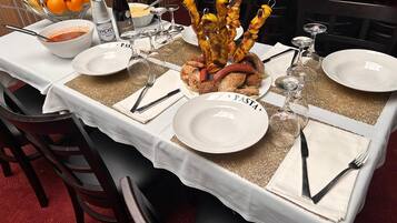 Una mesa de comedor dispuesta con platos, cubiertos y diversos alimentos, incluyendo brochetas y un bol de fruta.