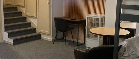 A hotel room with a bed, a desk, a chair, a television mounted on a wooden panel, and a staircase leading to another room.