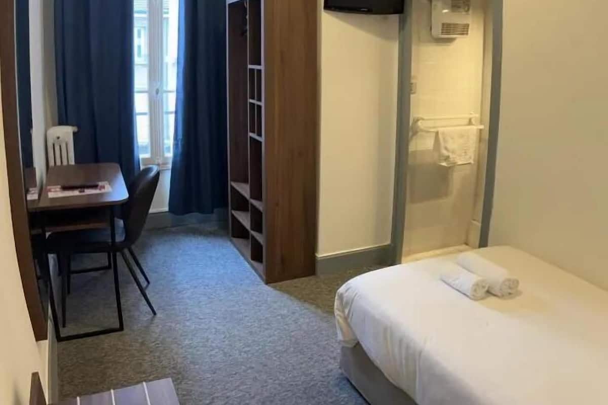 Hotelkamer met een bed, bureau, stoel, kast, televisie en douche.