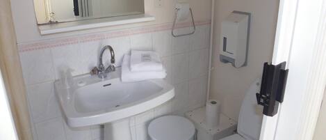 A small bathroom with a sink, mirror, towel, toilet, and a soap dispenser.