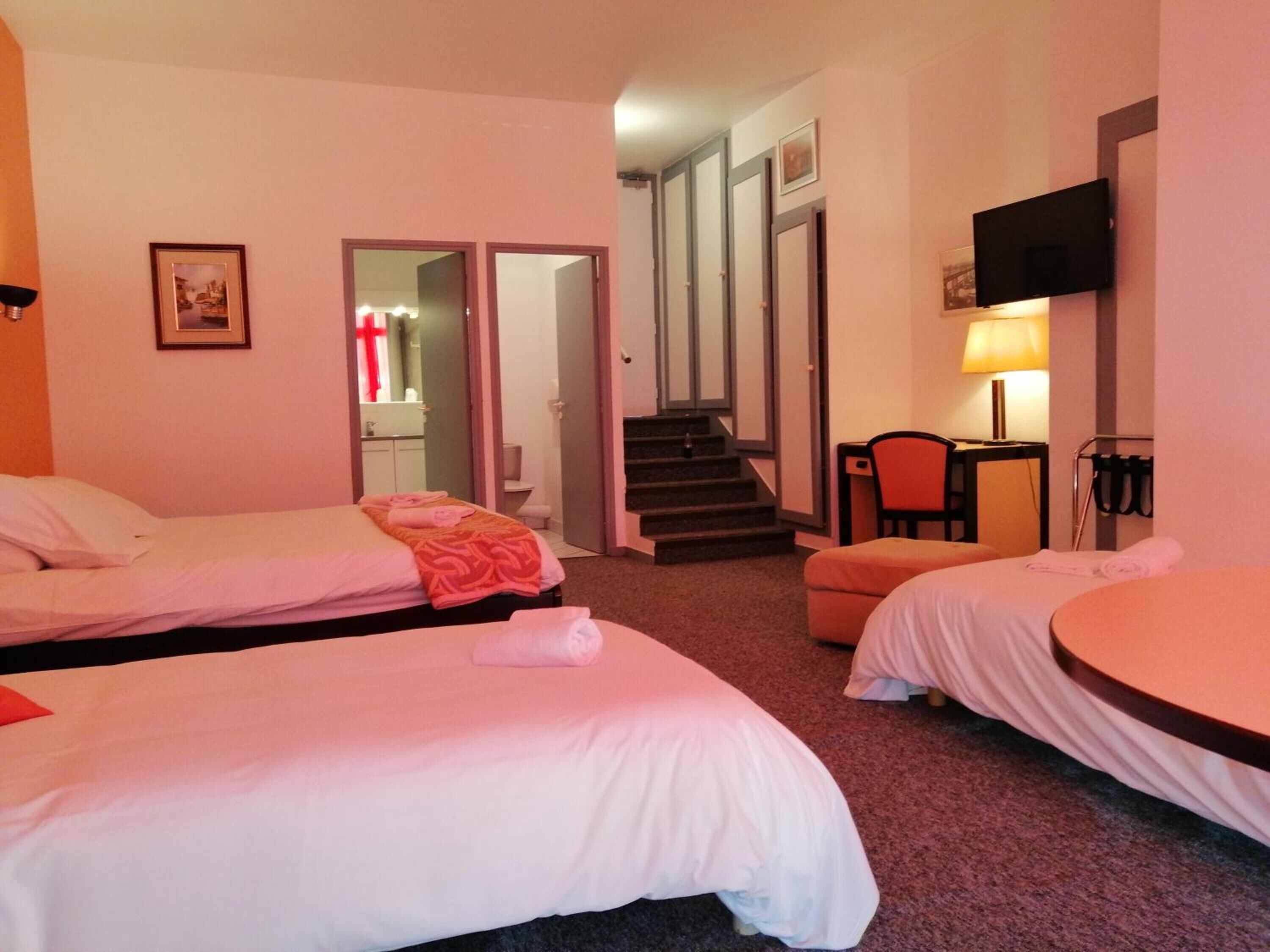 Une chambre d’hôtel avec deux lits simples, un bureau avec une chaise, un téléviseur fixé au mur et un escalier menant à une autre pièce.