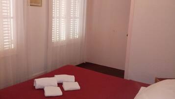Een hotelkamer met een rode sprei, witte kussens en een ingelijst schilderij aan de muur.