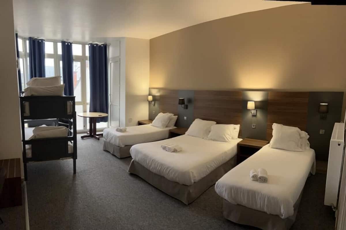 Een hotelkamer met drie eenpersoonsbedden, een klein bureau en een stoel.