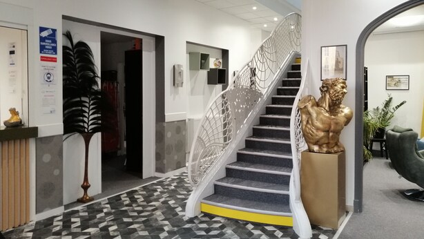 Een moderne hotel lobby met een vloer met geometrisch patroon, een witte trap met decoratief hekwerk en een gouden beeld.