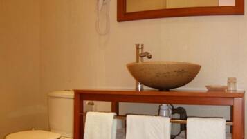 A bathroom with a wooden vanity, a large bowl sink, a toilet, and a mirror above the vanity.