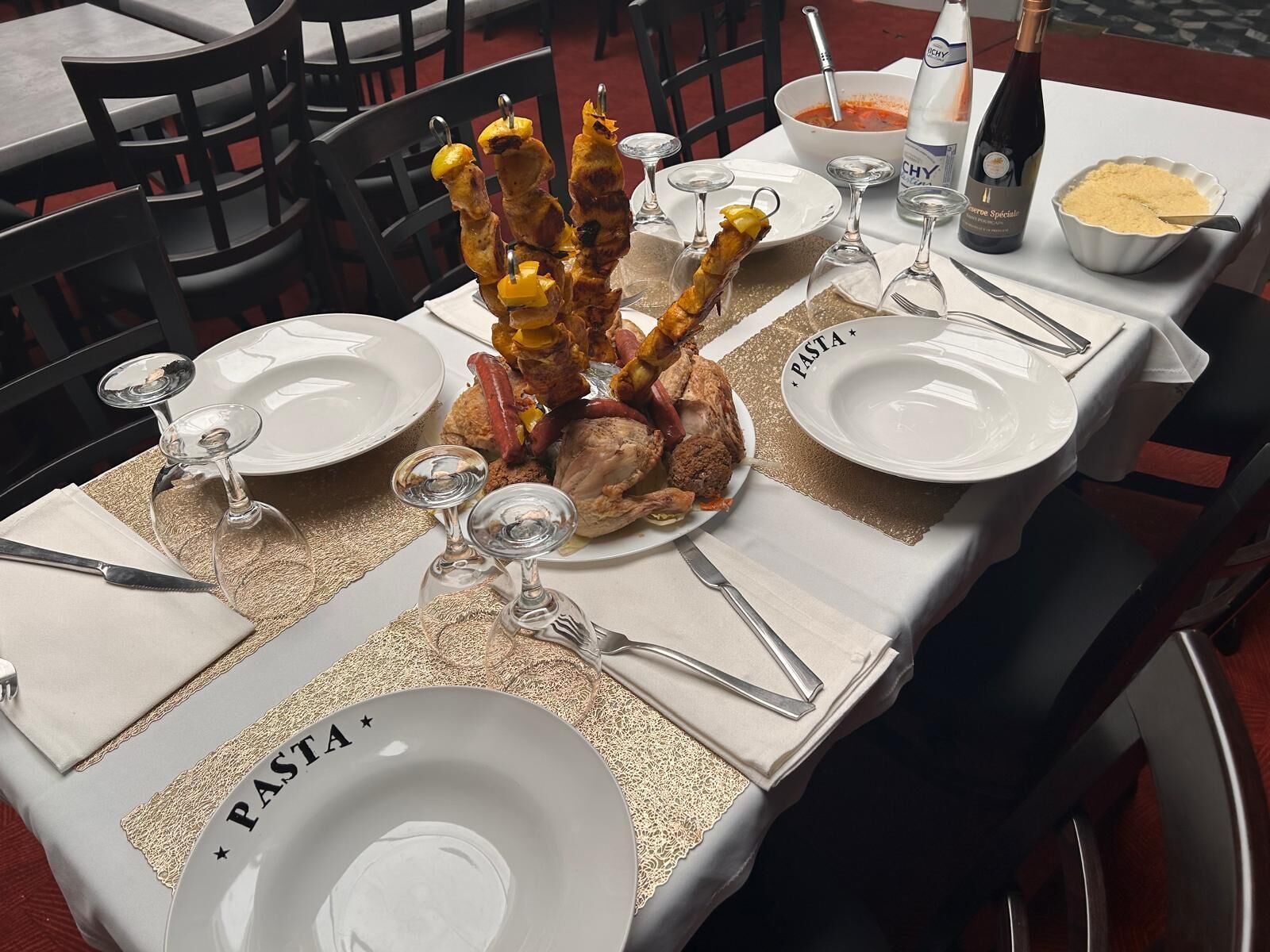 A dining table set with plates labeled "Pasta", a bottle of wine, and a bowl of pasta.