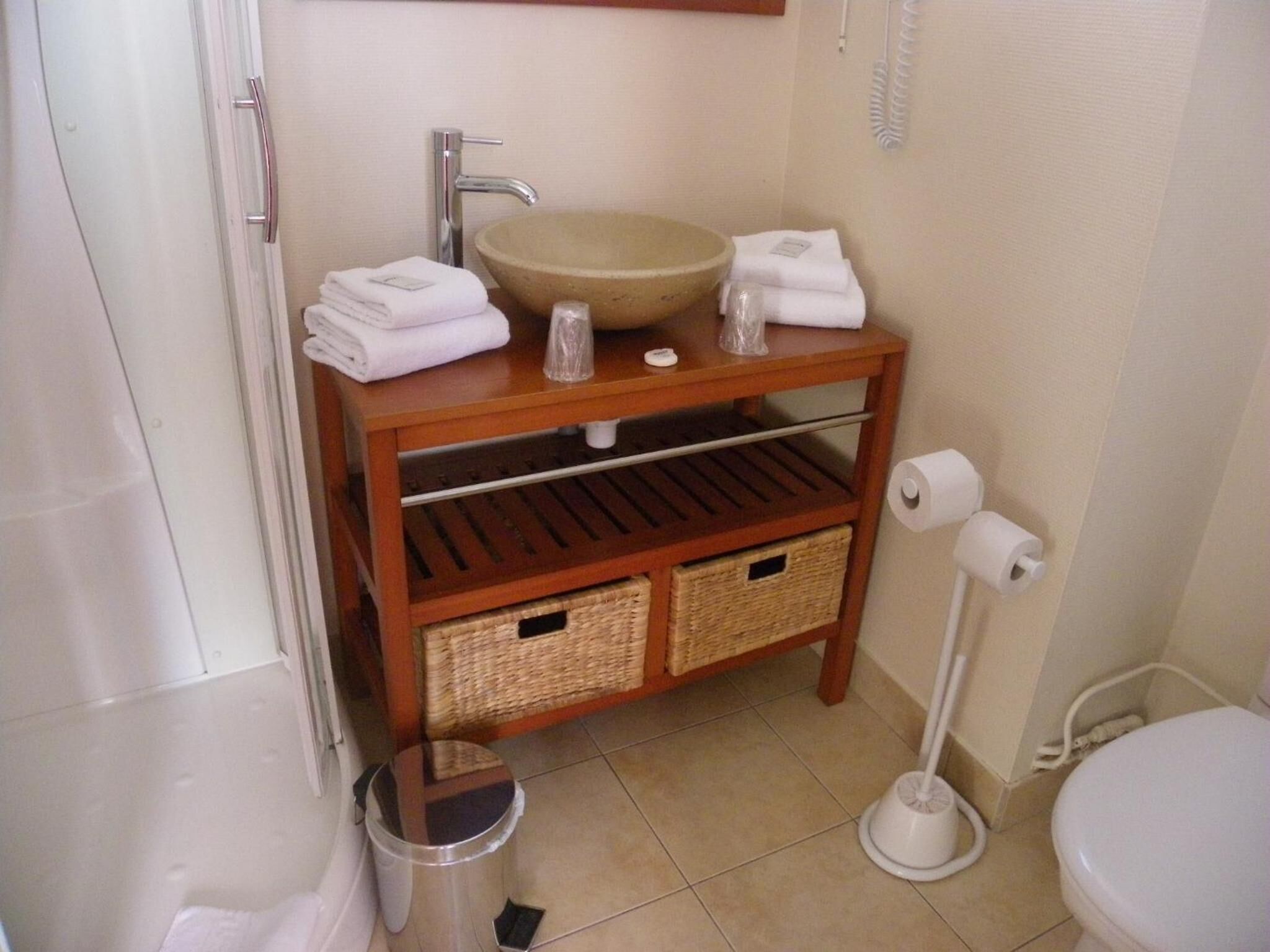 Un baño con un tocador de madera, un lavabo color beige y dos cestos de mimbre.
