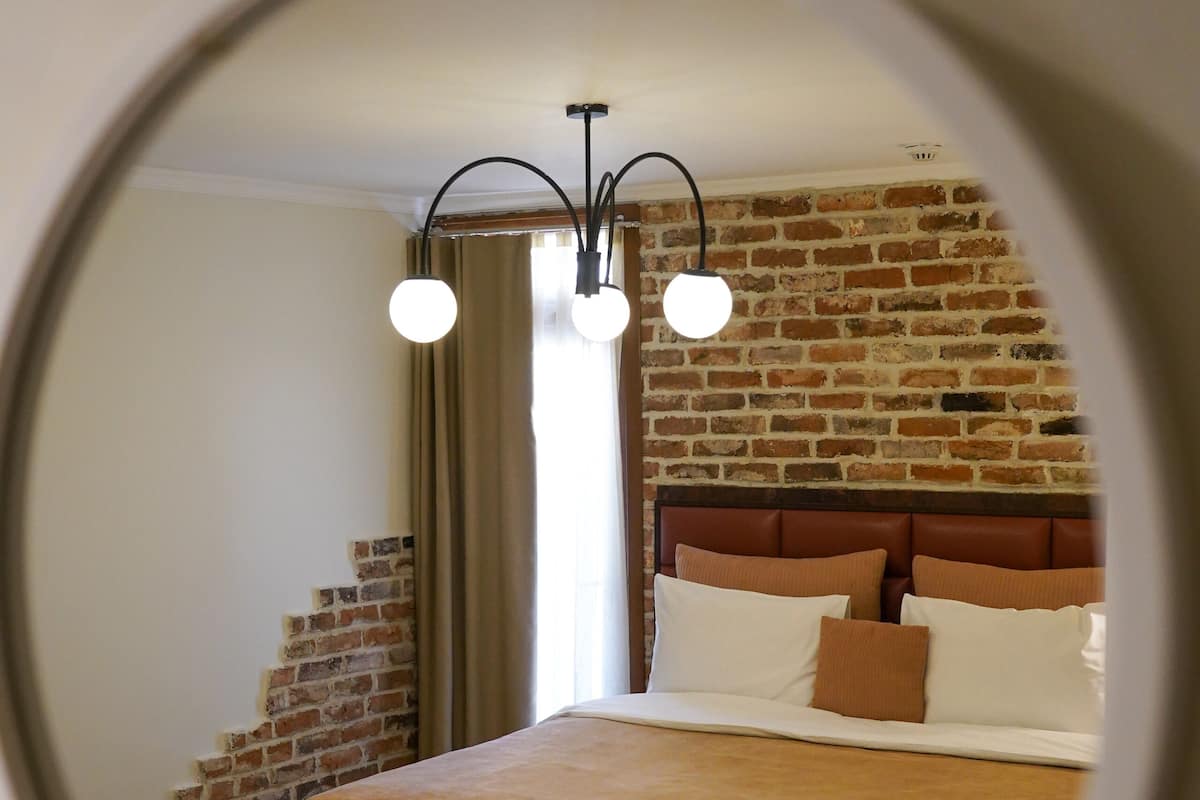 Une chambre avec un mur en briques, un lit doté d’une tête de lit marron et un miroir rond accroché au mur.