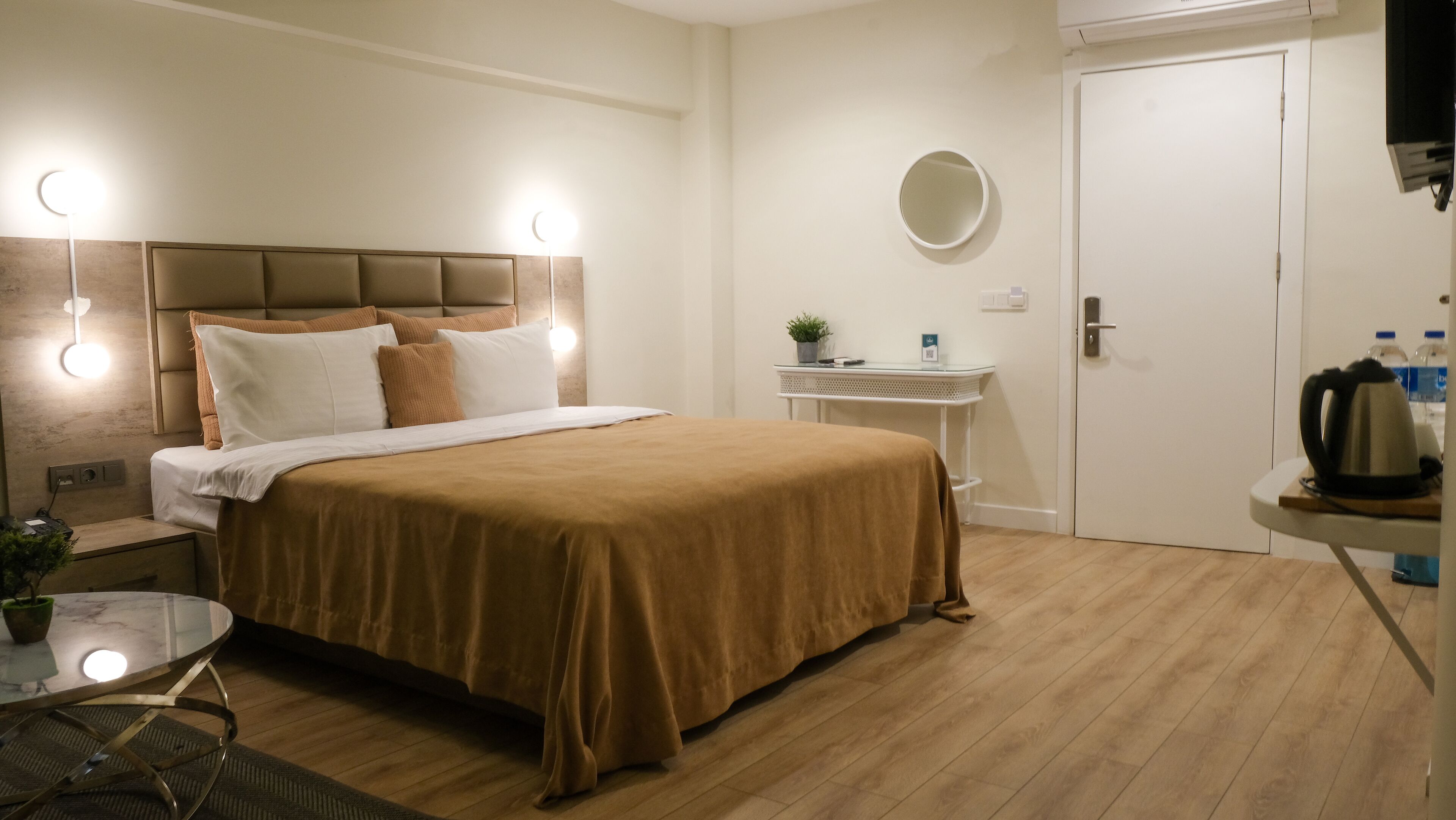 A neatly arranged bedroom with a bed, bedside table, and a small table with a kettle and water bottles.