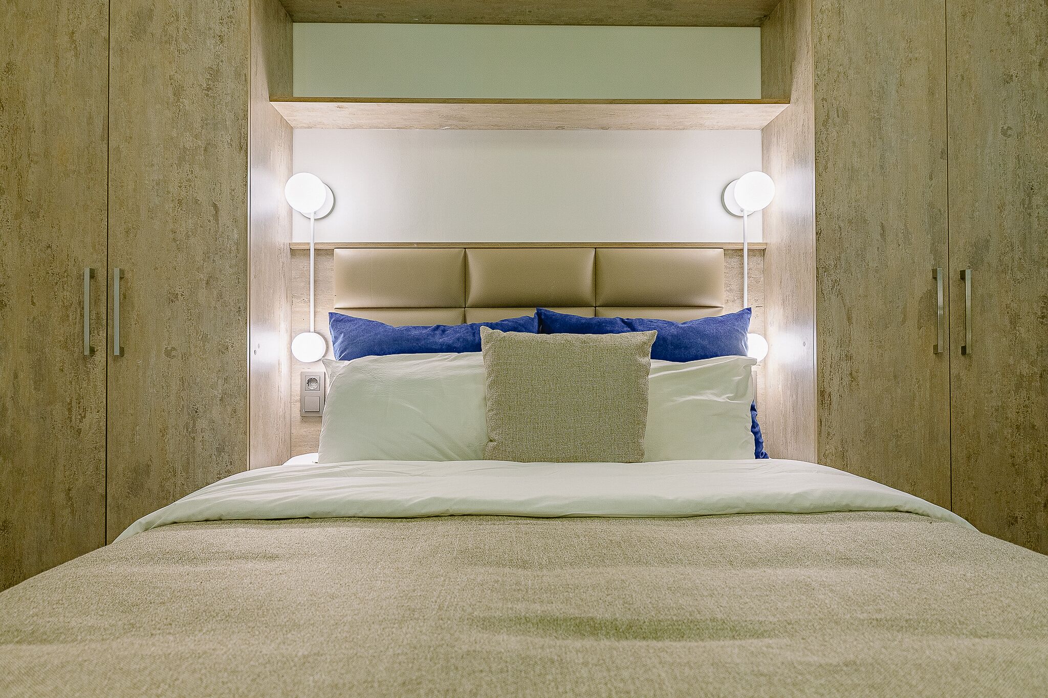 A bed with a headboard, bedside lamps, and a neutral-toned room.