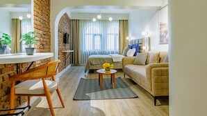 A living room with a brick wall, a sofa, a coffee table with flowers, a dining table with chairs, and a TV. - The Wilson Galata Hotel (Istanbul)