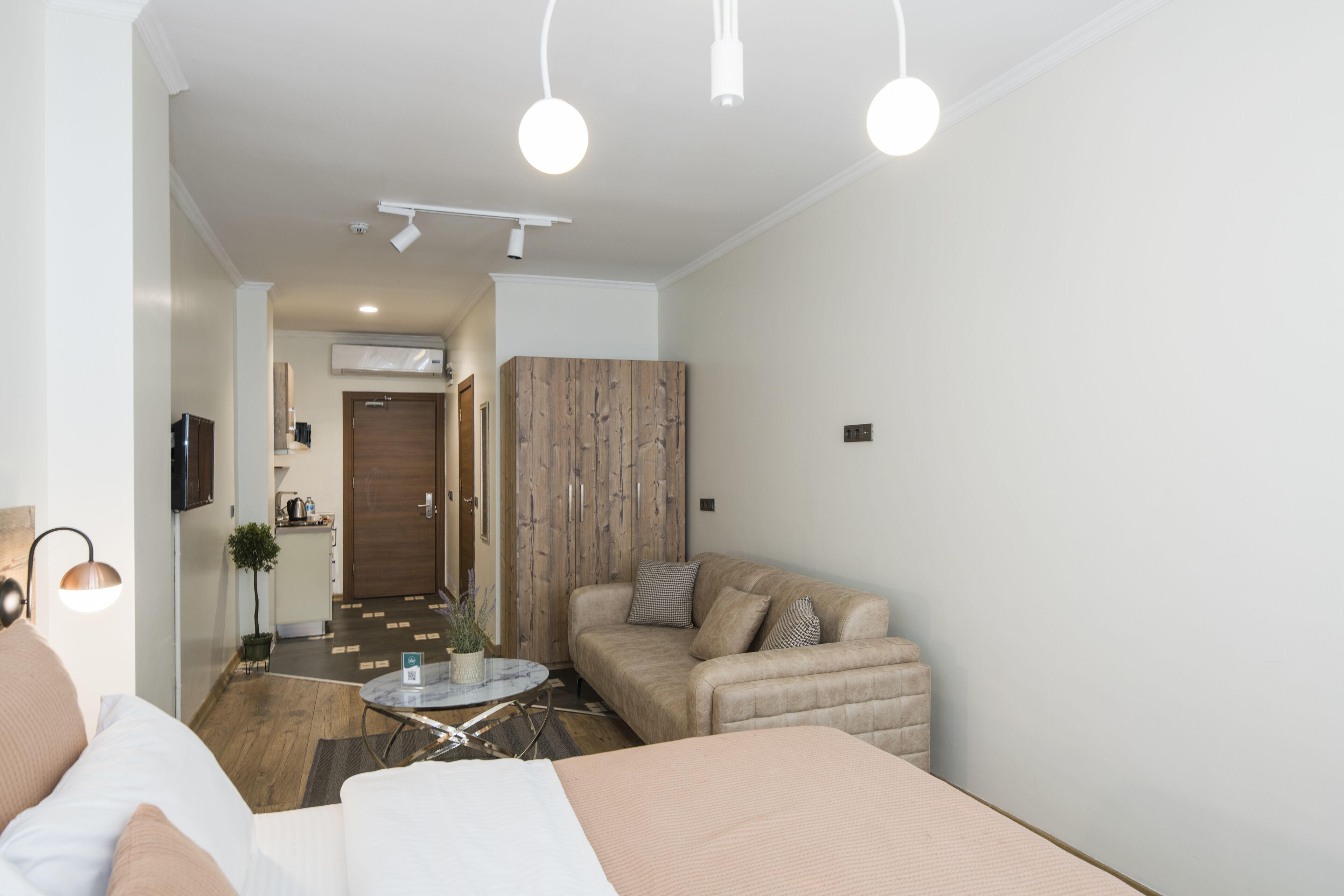 A modern hotel room with a bed, a sofa, a small table, and a wooden wardrobe.