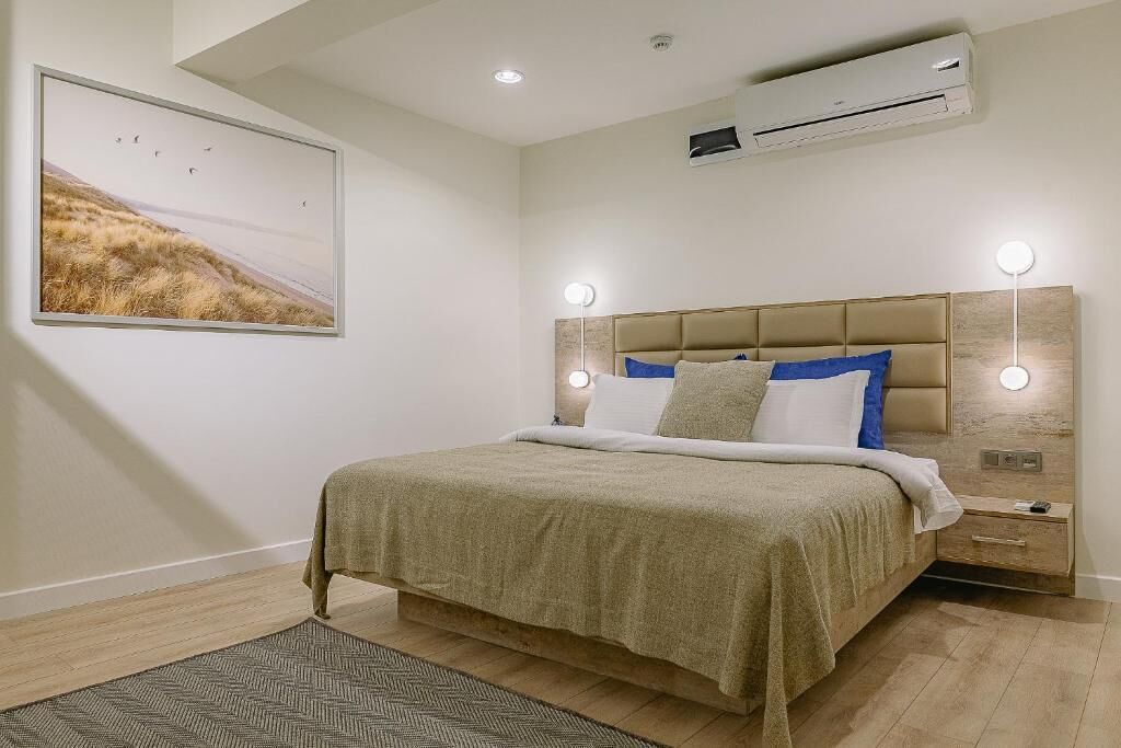 Een slaapkamer met een bed, nachtkastjes, een wandairconditioner en een ingelijst schilderij aan de muur.