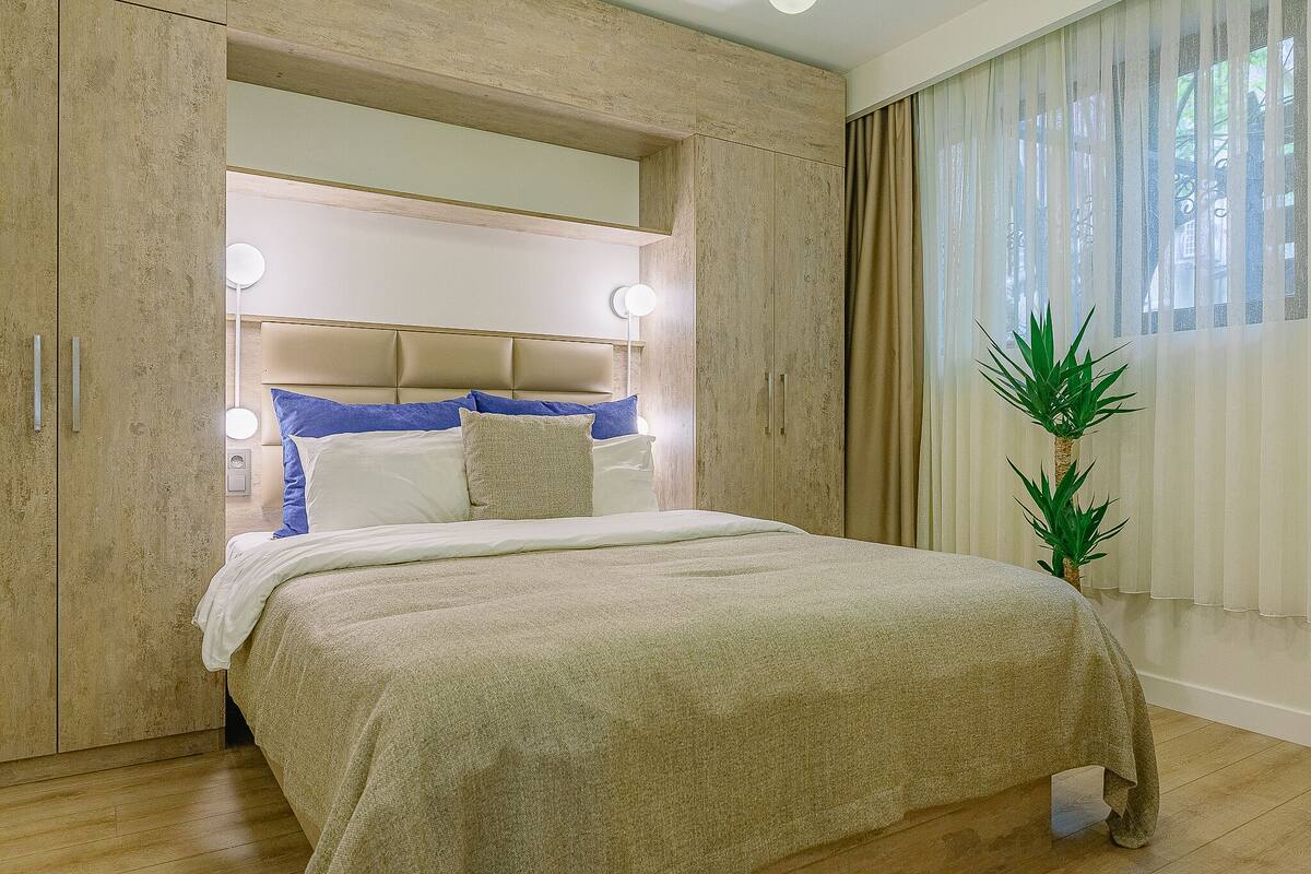 Une chambre à coucher avec un lit, des lampes de chevet, une plante en pot et une fenêtre avec des rideaux.