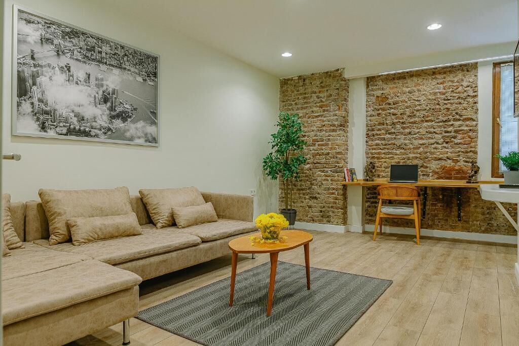 Una sala de estar con un sofá, una mesa de centro, un cuadro, un escritorio con una computadora y una pared de piedra.