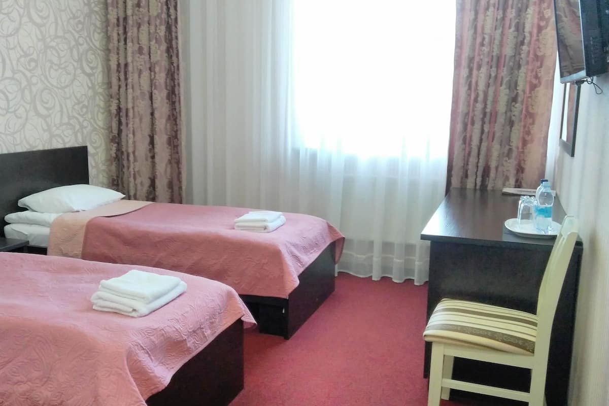 A hotel room with two beds, a desk, a chair, and a TV.