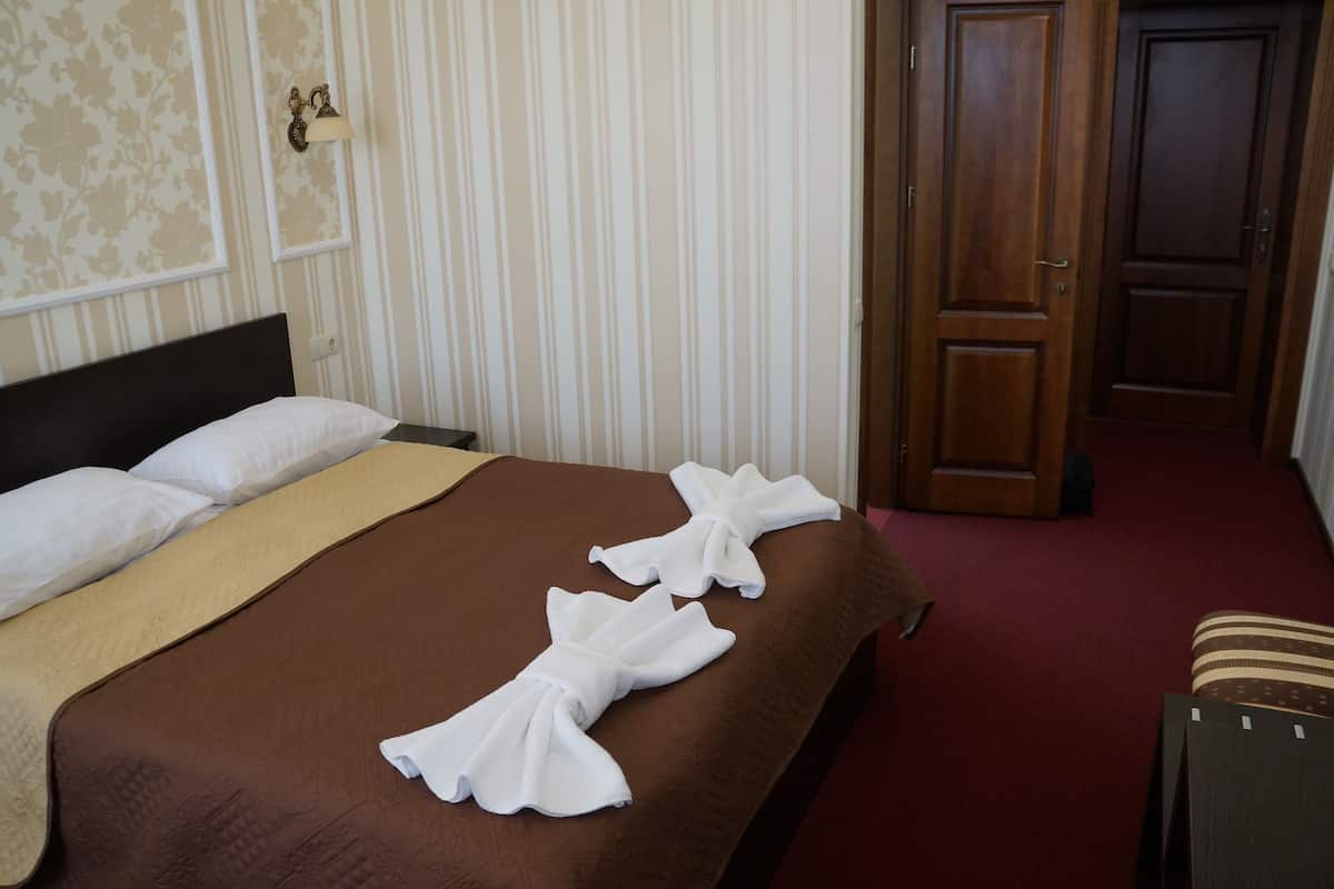 A hotel room with a neatly made bed, striped wallpaper, and a wooden door.