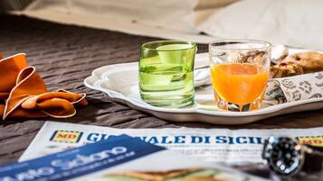 Bandeja de café da manhã com um copo de vidro verde, suco de laranja e doces sobre a cama, com um jornal e um relógio.