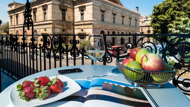 A table with a glass of white wine, a bowl of apples, and a plate of strawberries. - B&B In Centro Palermo (Palermo)