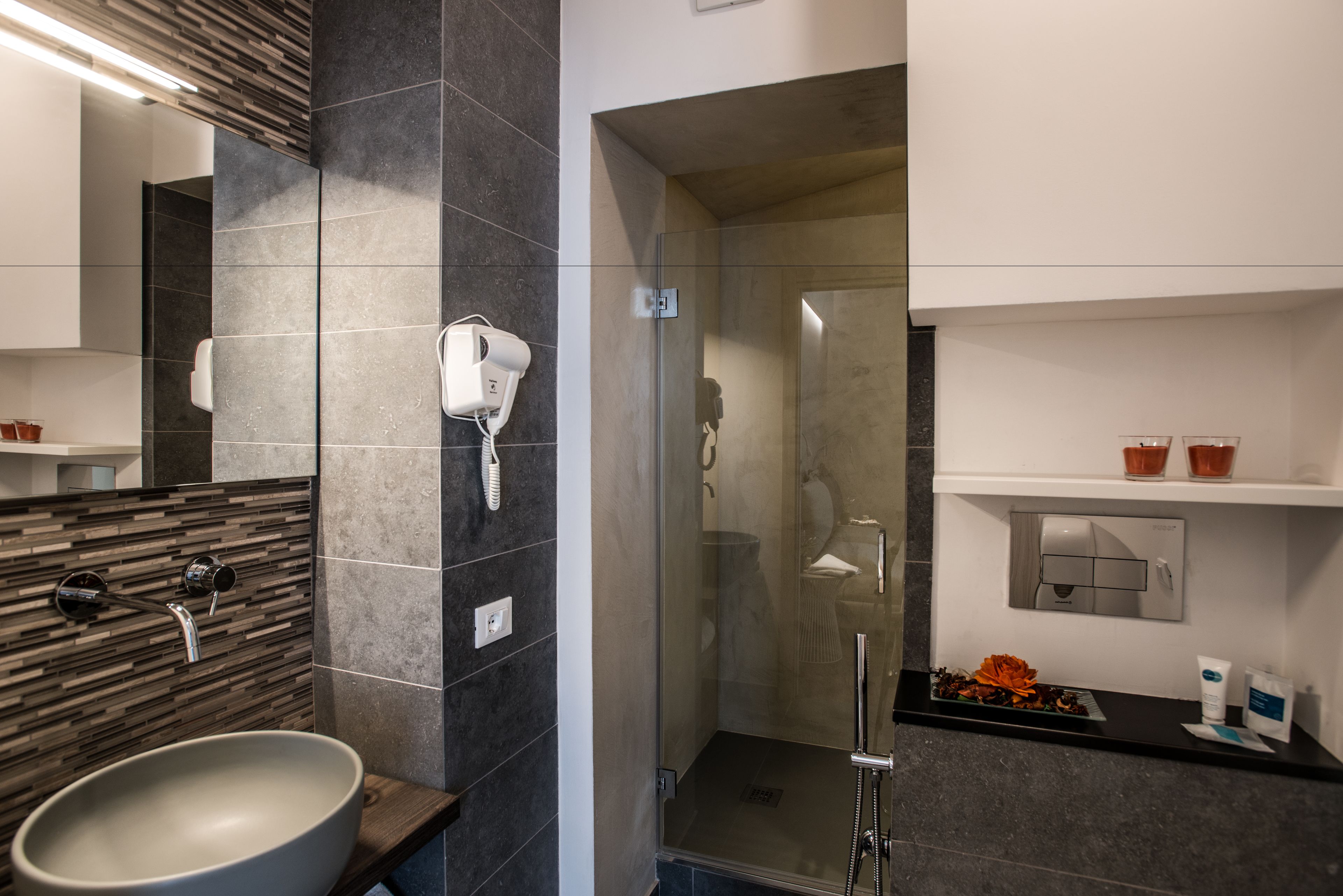 Ein modernes Badezimmer mit einem großen Waschbecken, einem Fön, einer Duschkabine und einem Ablagetisch mit Toilettenartikeln.