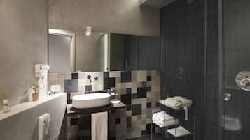 Un baño moderno con un espejo grande, un lavamanos y una zona de ducha con mampara de cristal.